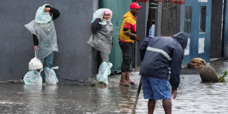 Residents walk across a flooded road following severe weather with heavy rain from a cold front in Masiphumelele, Cape Town, South Africa on May 20, 2025