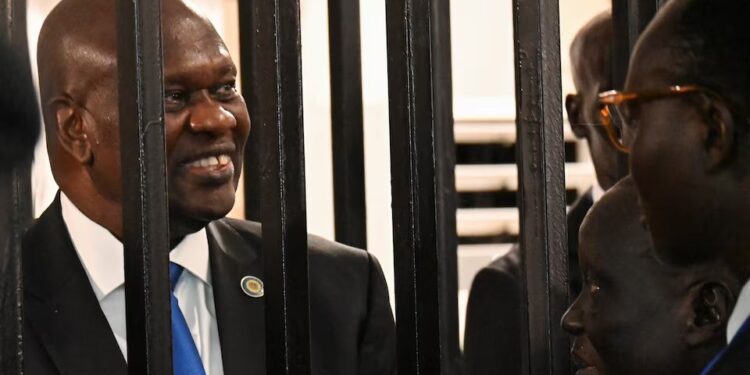 South Sudan’s suspended First Vice President Riek Machar stands inside a steel caged dock as he talks to his legal counsel before his trial on charges including treason and crimes against humanity, at the Freedom Hall in Juba, South Sudan