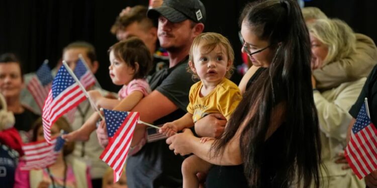 White South African refugees from South Africa holding American flags arrive, May 12, 2025, at Dulles International Airport in Dulles, Va.