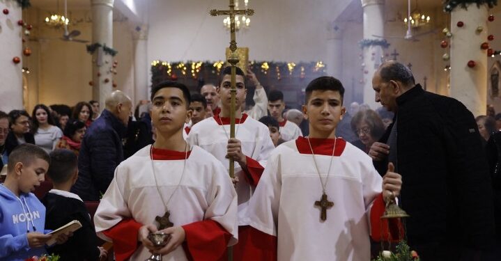 Altar servers and the cross bearer walk down the aisle during a Christmas Mass celebrated with displaced worshippers at the Roman Catholic Church of the Holy Family in Gaza City