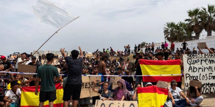 Migrants hold Spanish flags and signs calling for asylum as they gather in Ceuta, Spain, August 16, 2026